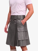 A gray faux-leather pleated kilt with a matching belt, side D-rings, and cargo pockets, shown on a model wearing a light pink t-shirt against a white background.