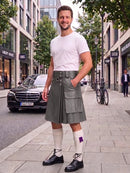 A man wearing a gray leather kilt, white t-shirt, white knee-high socks, and black leather shoes stands on a city sidewalk.