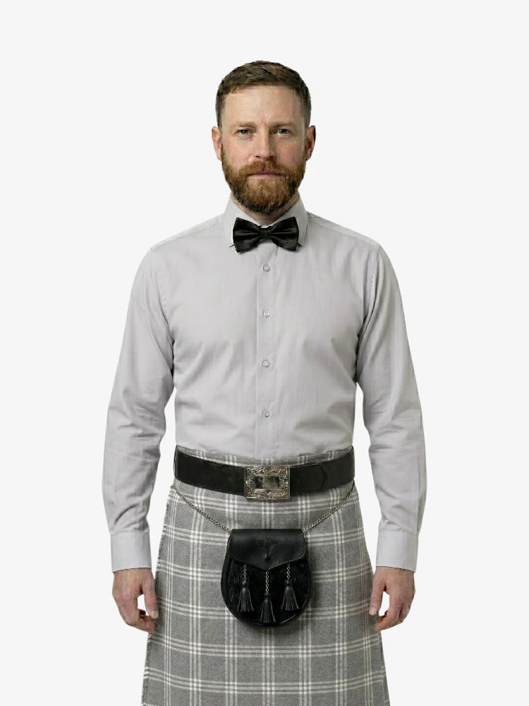 Man wearing a light gray shirt, black bow tie, and gray plaid kilt on a white background
