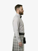 Man wearing a light gray dress shirt, black belt, and plaid kilt on a white background