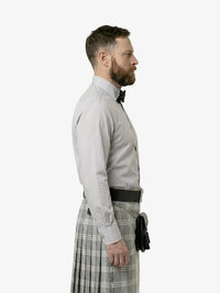 Man wearing a light gray dress shirt, black belt, and plaid kilt on a white background