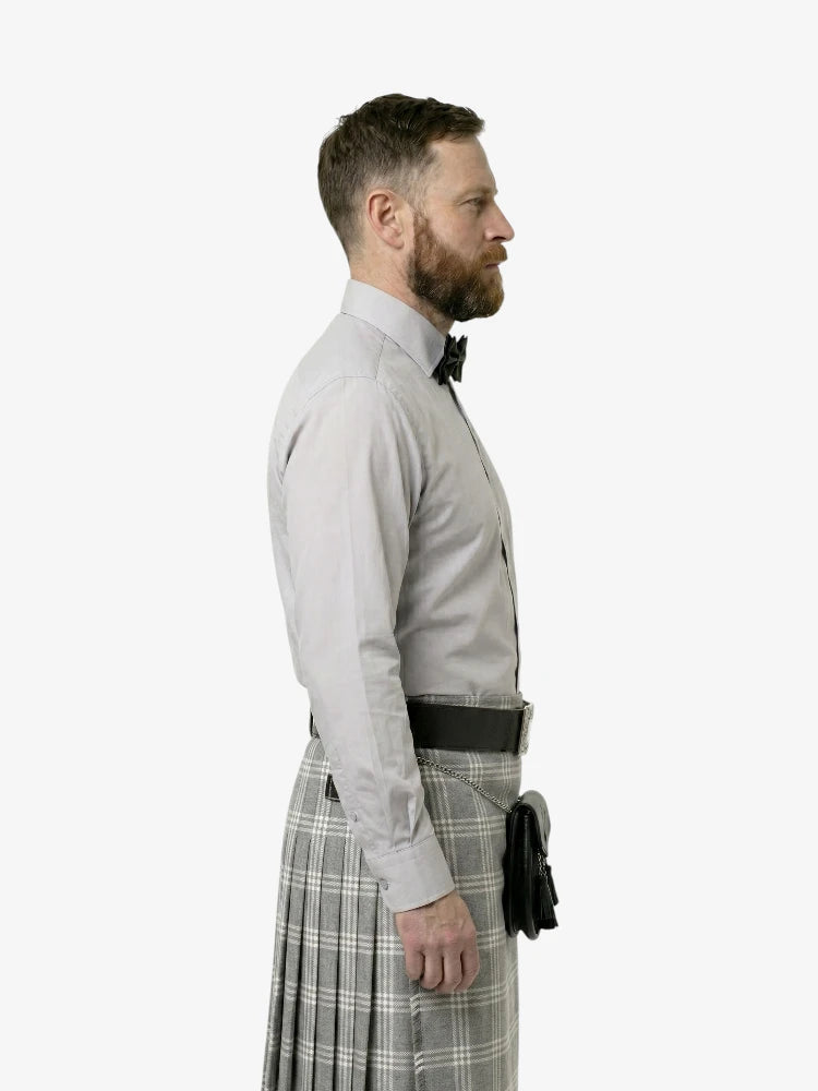 Man wearing a light gray dress shirt, black belt, and plaid kilt on a white background