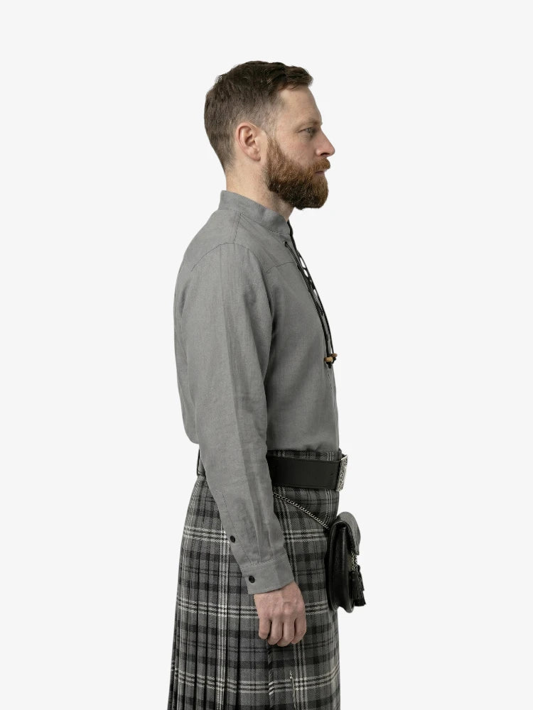 Man wearing a gray shirt and plaid kilt on a white background