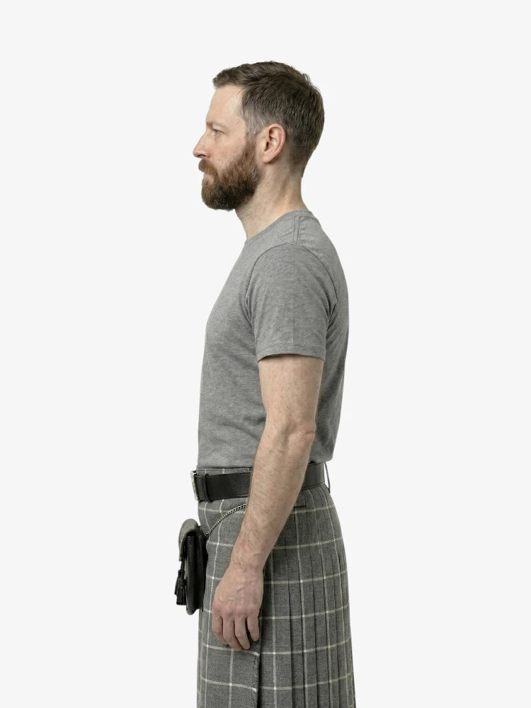 Man wearing a gray t-shirt and plaid kilt on a white background