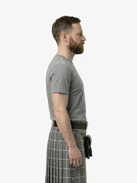 Man wearing a gray t-shirt and plaid kilt on a white background
