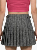 Person wearing a gray pleated skirt with a pink top on a white background