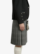 Person wearing a black blazer and gray pleated kilt on a white background