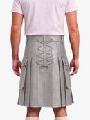 A person shown from the back wearing a light gray pleated faux-leather kilt with a lace-up back closure, side flap pockets, and a matching belt, paired with a pale pink t-shirt.