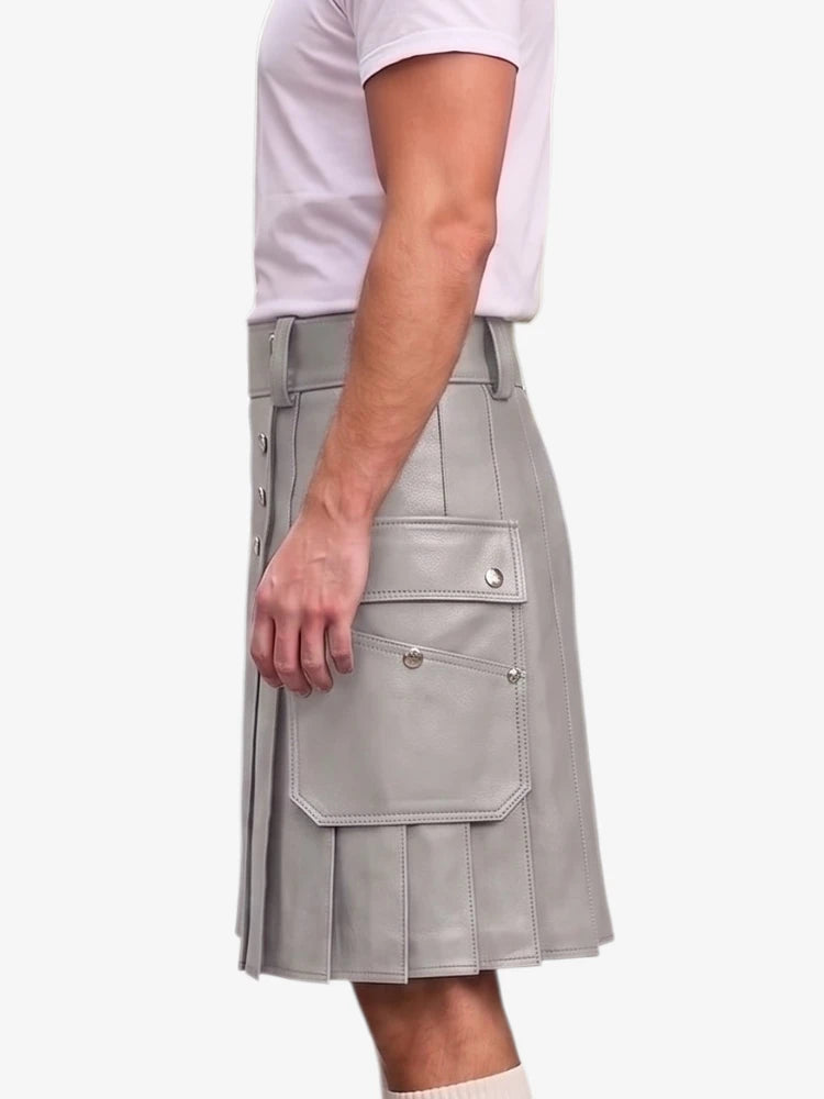 A side view of a person wearing a light gray pleated faux-leather kilt with flap pockets and silver snap details, paired with a white t-shirt, against a plain light gray background.