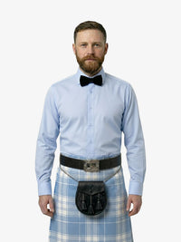Man wearing a light blue shirt, black bow tie, and plaid kilt on a white background