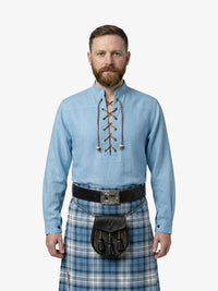 Man wearing a light blue shirt with lace-up details and a plaid kilt on a white background