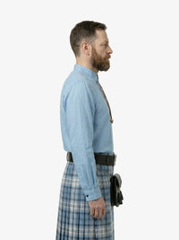 Man wearing a light blue shirt and plaid kilt on a white background