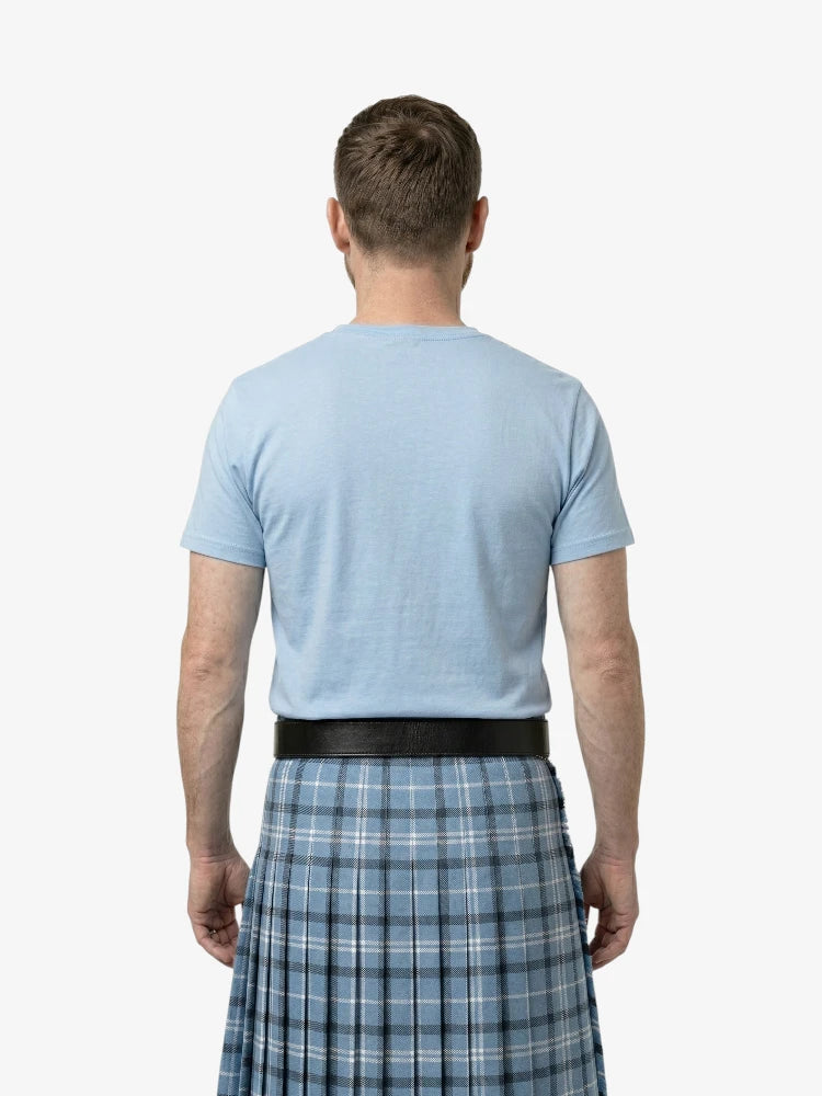 Man wearing a light blue t-shirt and plaid kilt on a white background