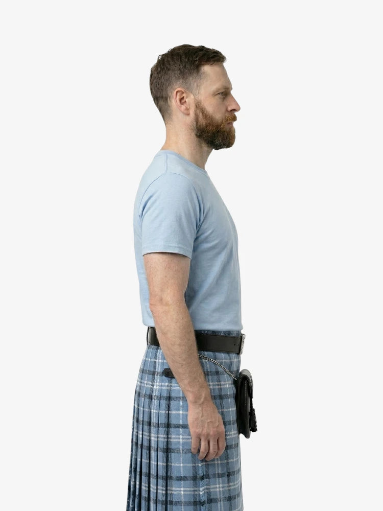 Man wearing a light blue t-shirt and plaid kilt on a white background