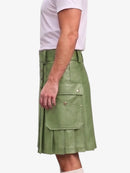 A side view of a person wearing a sage green faux-leather kilt with flap pockets and gold-tone hardware, paired with a white t-shirt against a light gray background.