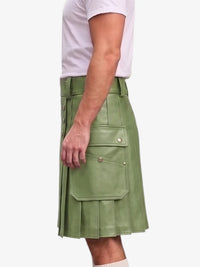 A side view of a person wearing a sage green faux-leather kilt with flap pockets and gold-tone hardware, paired with a white t-shirt against a light gray background.