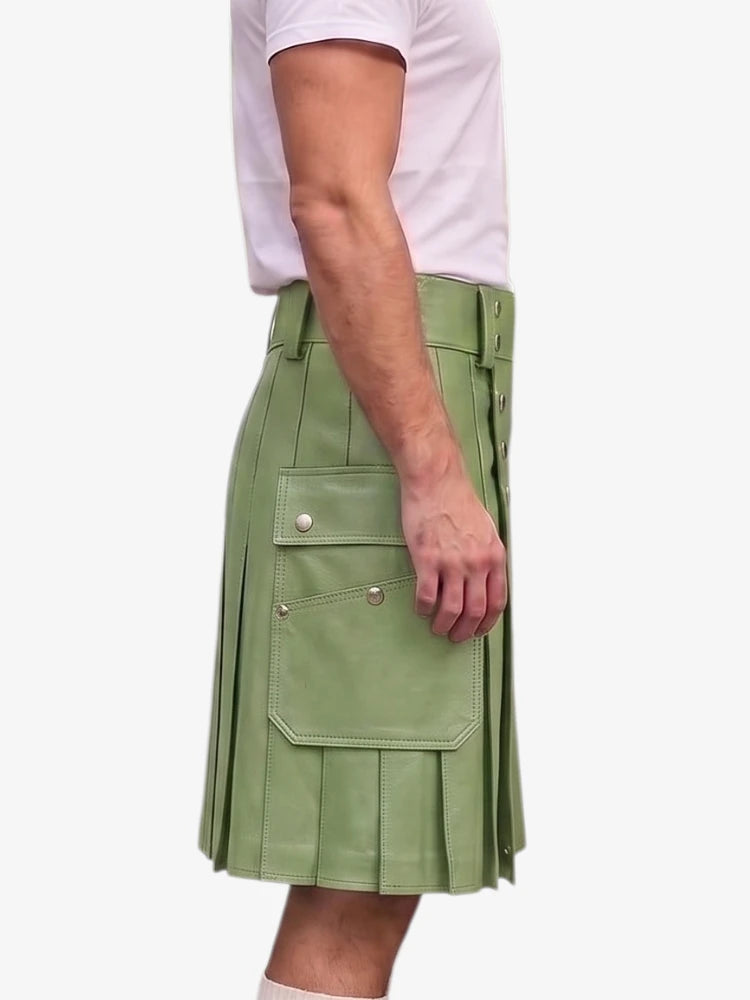 A person wearing a sage green faux-leather kilt with pleated detailing, flap pockets, and silver snap buttons, paired with a light pink t-shirt, shown from the side against a plain white background.