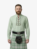Man wearing a light green shirt with lace-up front and a green plaid kilt on a white background