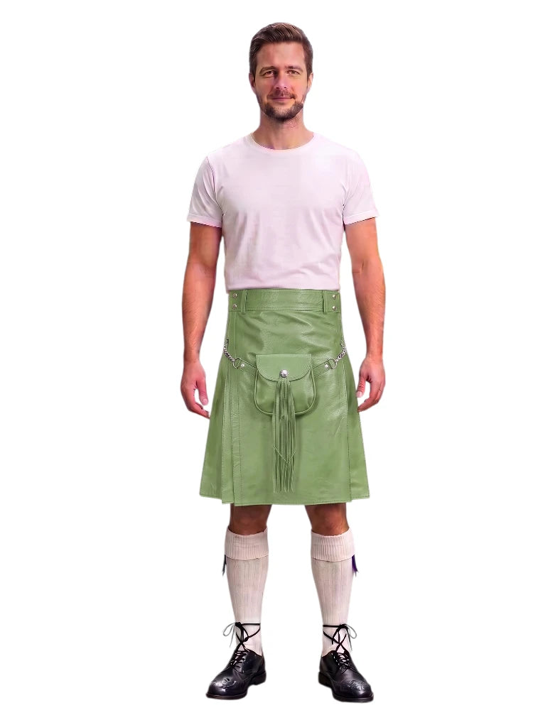 A man modeling a light green faux-leather kilt with silver hardware, paired with a white t-shirt, cream knee-high socks, and black lace-up shoes, against a plain white background.