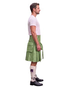 A man shown in profile wearing a light green kilt, a white t-shirt, white knee-high socks, and black leather shoes, photographed against a solid white background.