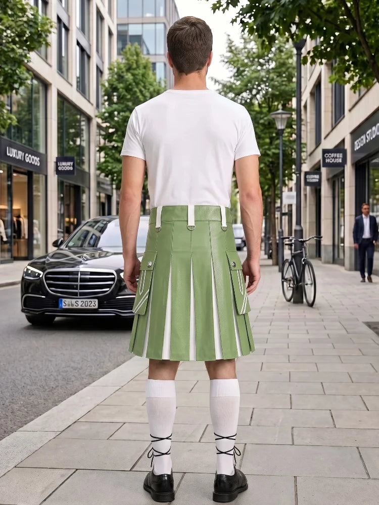 A man stands on a city sidewalk facing away from the camera, wearing a white short-sleeve T-shirt and a light green pleated kilt with white vertical stripe details. He is also wearing white knee-high socks and black shoes.