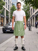 A man stands on a city sidewalk wearing a white crew-neck t-shirt and a light green kilt with white geometric stripe patterns. He is styled with white knee-high socks and black leather oxford shoes, with a street scene featuring a Mercedes-Benz and storefronts in the background.