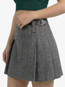 Person wearing a black and white herringbone patterned skirt with a green top on a white background