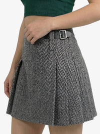 Person wearing a black and white herringbone patterned skirt with a green top on a white background