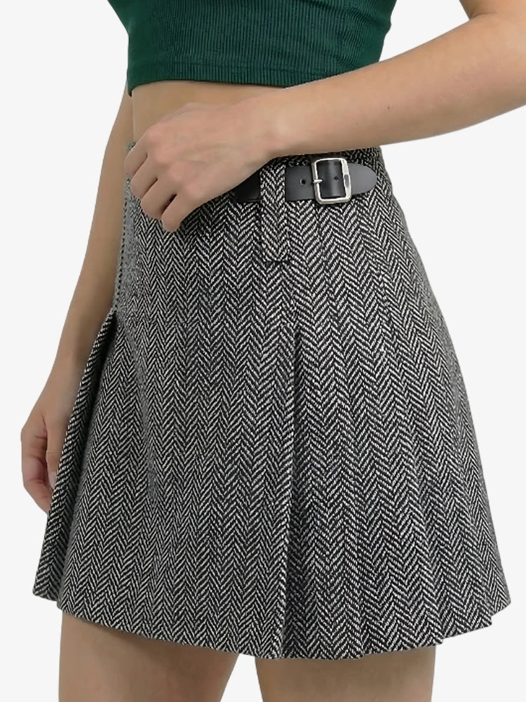 Person wearing a black and white herringbone patterned skirt with a green top on a white background