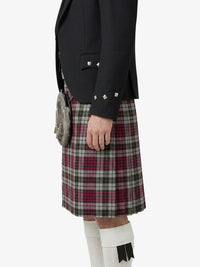 Person wearing a black jacket and plaid kilt on a white background