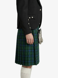 Person wearing a black blazer and green plaid kilt on a white background