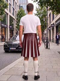 A man standing on a city sidewalk, viewed from behind, wearing a white t-shirt, a dark brown pleated leather kilt with white vertical stripes, white knee-high socks, and black shoes. Buildings, trees, a black Mercedes-Benz car, and a bicycle are visible in the background.