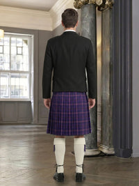 Man wearing a dark jacket and purple plaid kilt in an elegant room with columns.