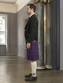 Man in formal attire with a purple kilt standing in an elegant interior setting.