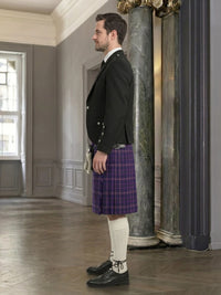 Man in formal attire with a purple kilt standing in an elegant interior setting.