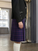 Person wearing a black jacket and purple plaid kilt indoors.