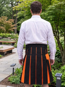 A man viewed from behind wearing a white long-sleeve dress shirt and a black pleated kilt with bright orange vertical stripes and a matching orange pocket, standing in a garden setting.