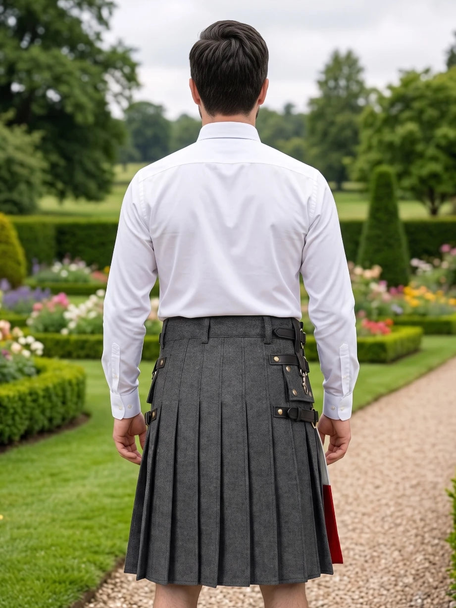 A man viewed from behind wearing a white dress shirt and a dark gray pleated kilt with black and gold buckle details, standing on a garden path.