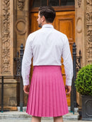 A man viewed from behind wearing a bright pink pleated kilt and a white long-sleeve dress shirt, standing in front of a stone building with a wooden door.