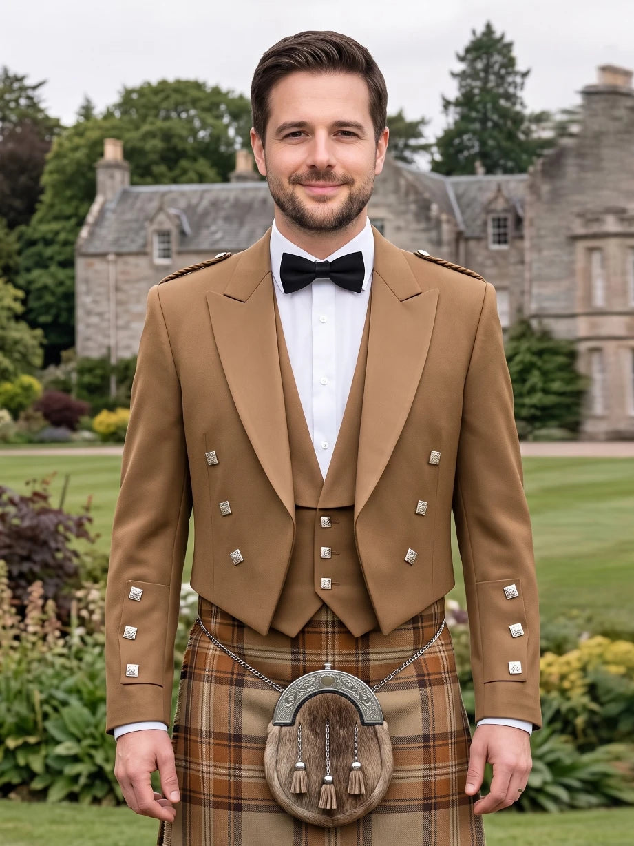 A man wearing a traditional Scottish formal outfit with a tan jacket, white shirt, black bow tie, and a brown tartan kilt with a sporran, standing outdoors in front of a stone mansion.