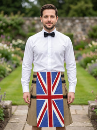A man standing in a garden wearing a white long-sleeve dress shirt, black bow tie, and a tan kilt with a large Union Jack flag design on the front panel.