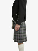 Person wearing a black blazer and plaid kilt on a white background