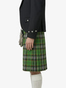 Person wearing a black jacket and green plaid kilt on a white background