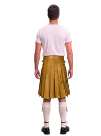A man shown from the back wearing a mustard yellow pleated leather kilt, a light pink t-shirt, white knee-high socks, and black shoes, isolated on a white background.