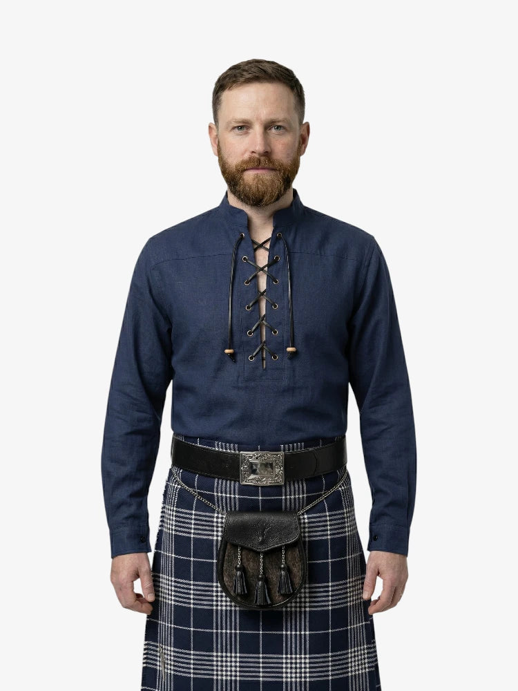 Man wearing a blue shirt with lace-up front and a plaid kilt on a white background
