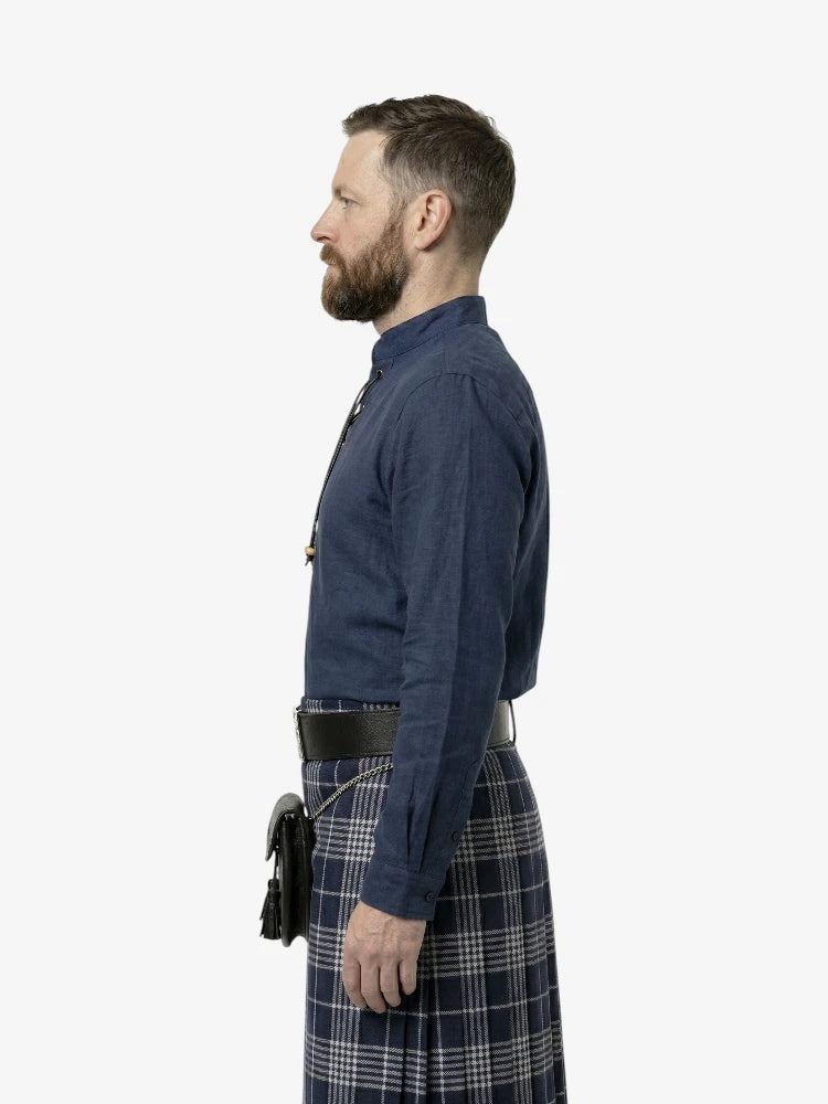 Man wearing a blue shirt and plaid kilt on a white background