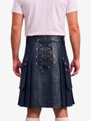 A man wearing a dark navy blue faux-leather kilt with a lace-up back closure, side pockets, and pleated front panels, paired with a light pink t-shirt and white socks.