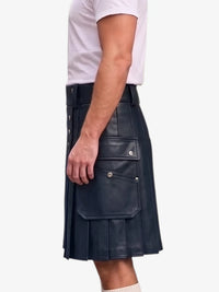 A man wearing a dark navy blue faux-leather kilt with pleats and front utility pockets, paired with a white t-shirt, shown from the side against a light gray background.