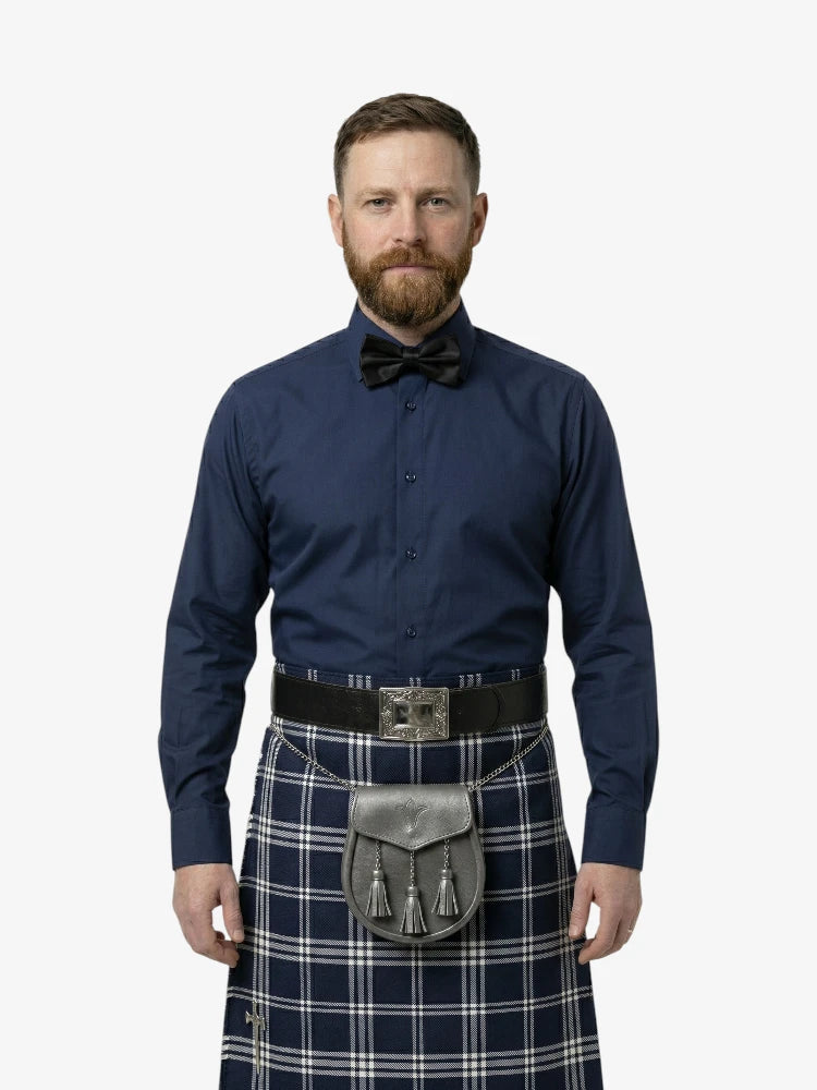Man wearing a navy shirt, bow tie, and tartan kilt on a white background