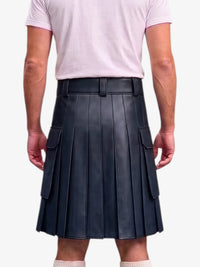 A person shown from the back wearing a black pleated leather kilt with side cargo pockets, paired with a light pink t-shirt and white socks, against a plain light gray background.